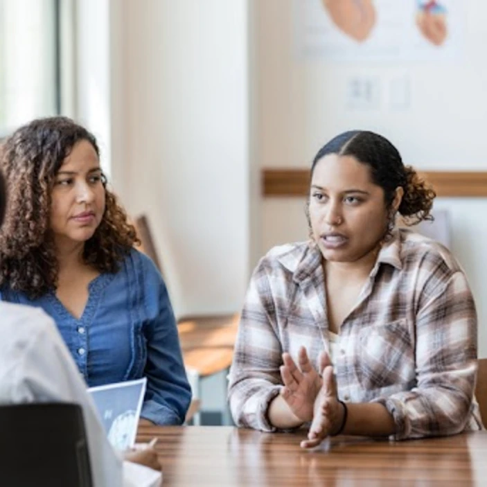 Deux femmes discutent avec une professionnelle dans un bureau lors d’une rencontre de type conseil d’école.